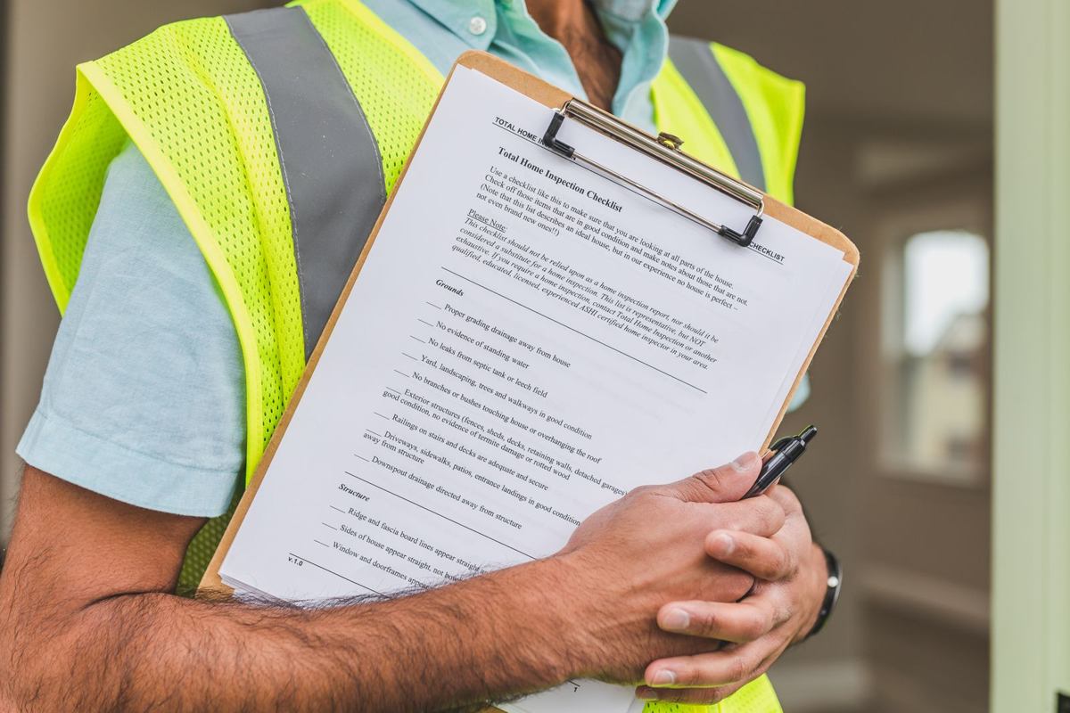 Home inspector in a safety vest holding a clipboard with a house inspection checklist, the report where a high radon result usually first appears